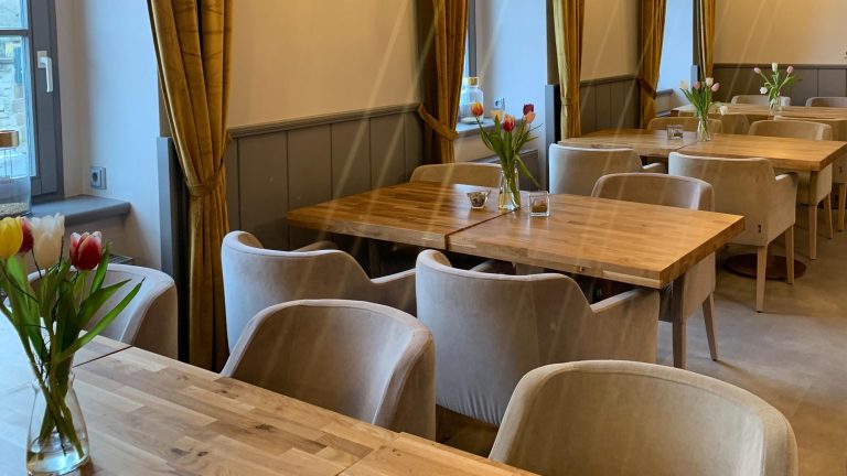 Blick auf den stilvollen Sitzbereich im Frühstücksraum des Hotel zur Kaiserpfalz mit Holztischen, gepolsterten Stühlen und dekorativen Blumenvasen.